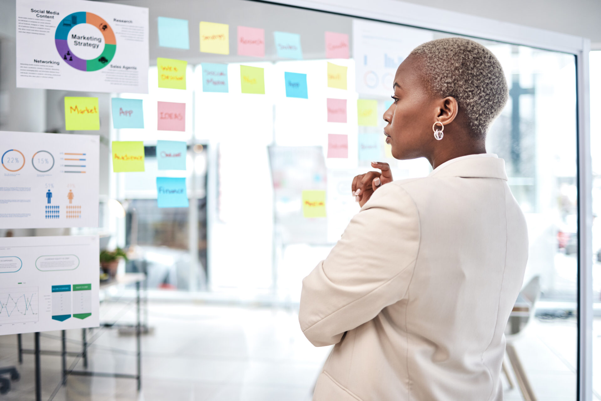 Black woman, thinking and glass board for project management, marketing or planning at office. African female person, manager or employee checking project plan, tasks or statistics at the workplace
